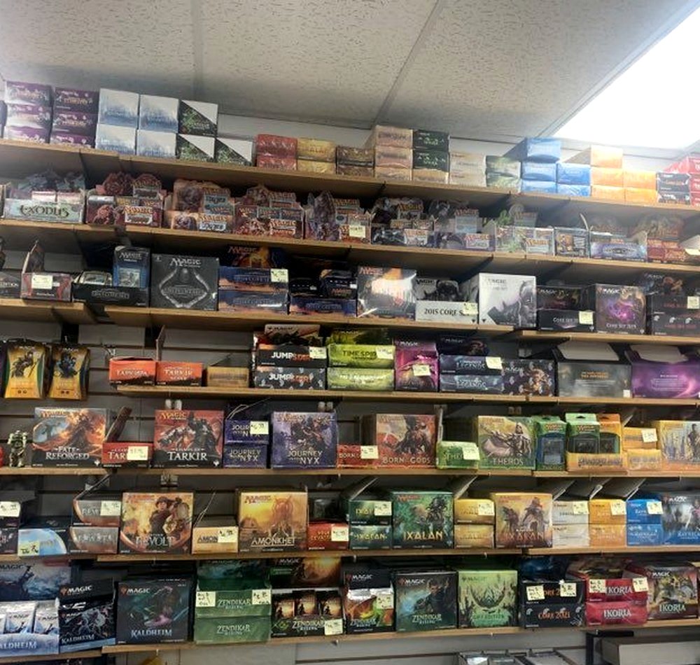 Wooden shelving from floor to ceiling filled with boxed card sets and board games, price tags handwritten on the shelf edges.