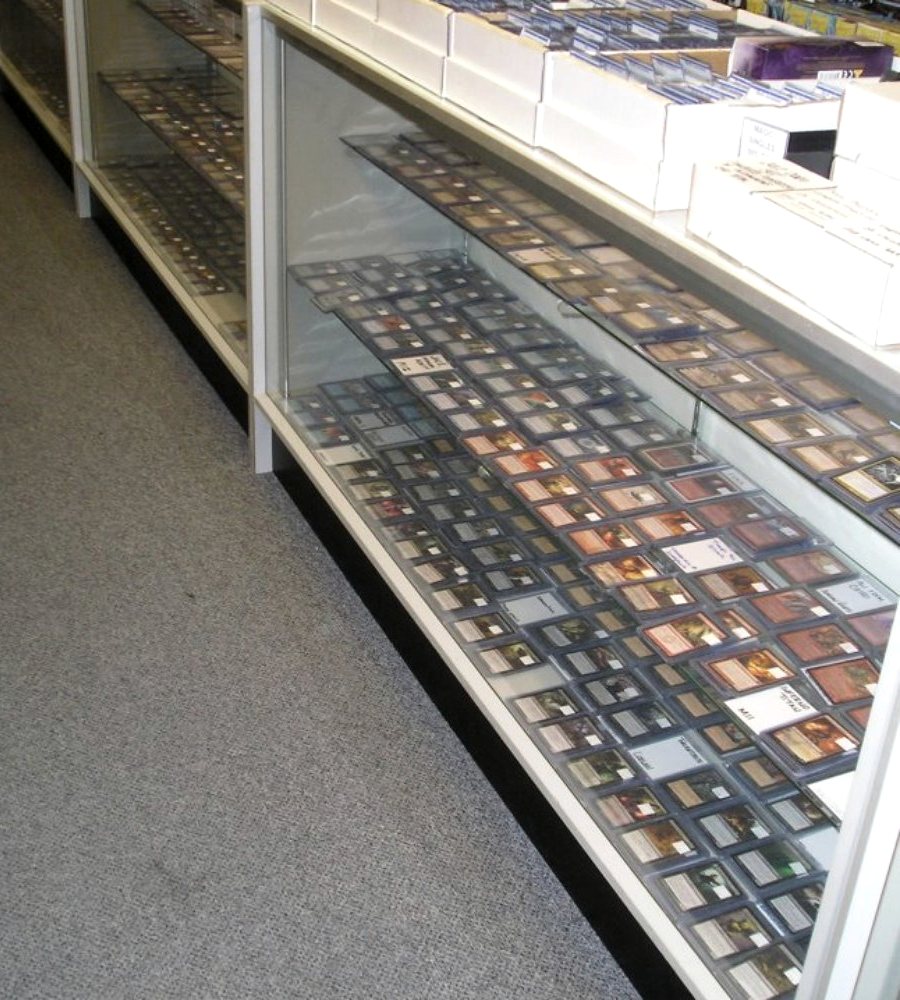 A long glass display case of sleeved single cards laid out in rows, white sorting boxes stacked on the counter above it.