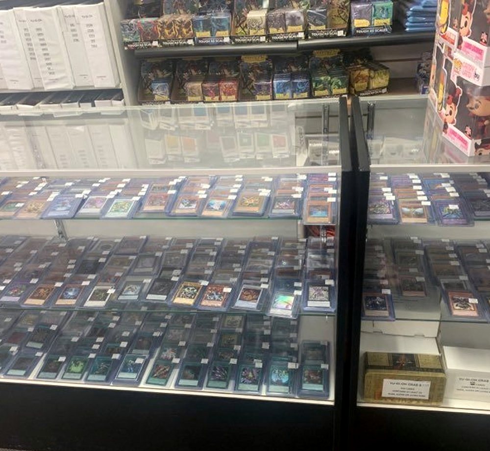 Rows of sleeved single cards standing upright in a lit glass counter, each with a small price tag.